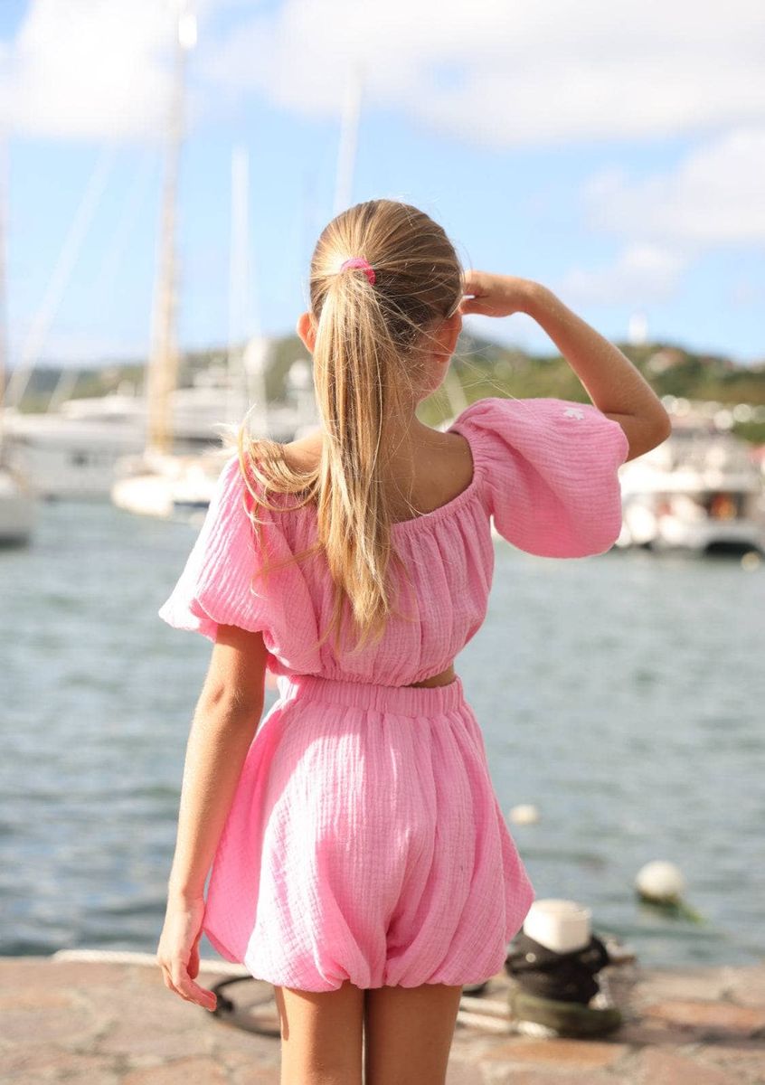 young girl in pink lola and the boys short and bubble top outfit standing by a waterfront with boats in the background