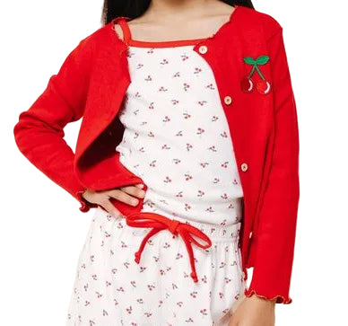Young girl wearing a red cardigan and white patterned pants on a beige background