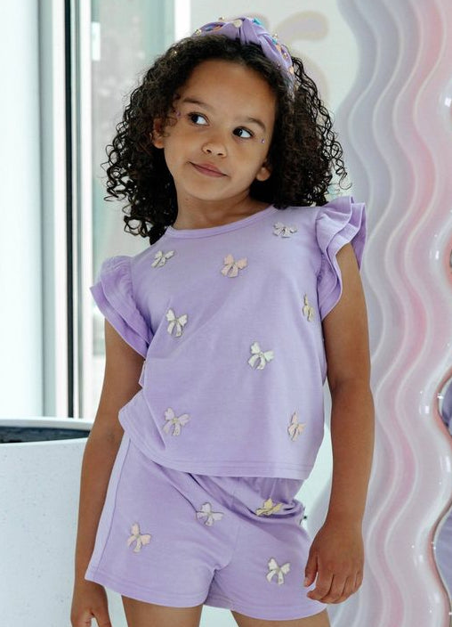 Young girl in a purple bow outfit from lola and the boys standing in front of a mirror.