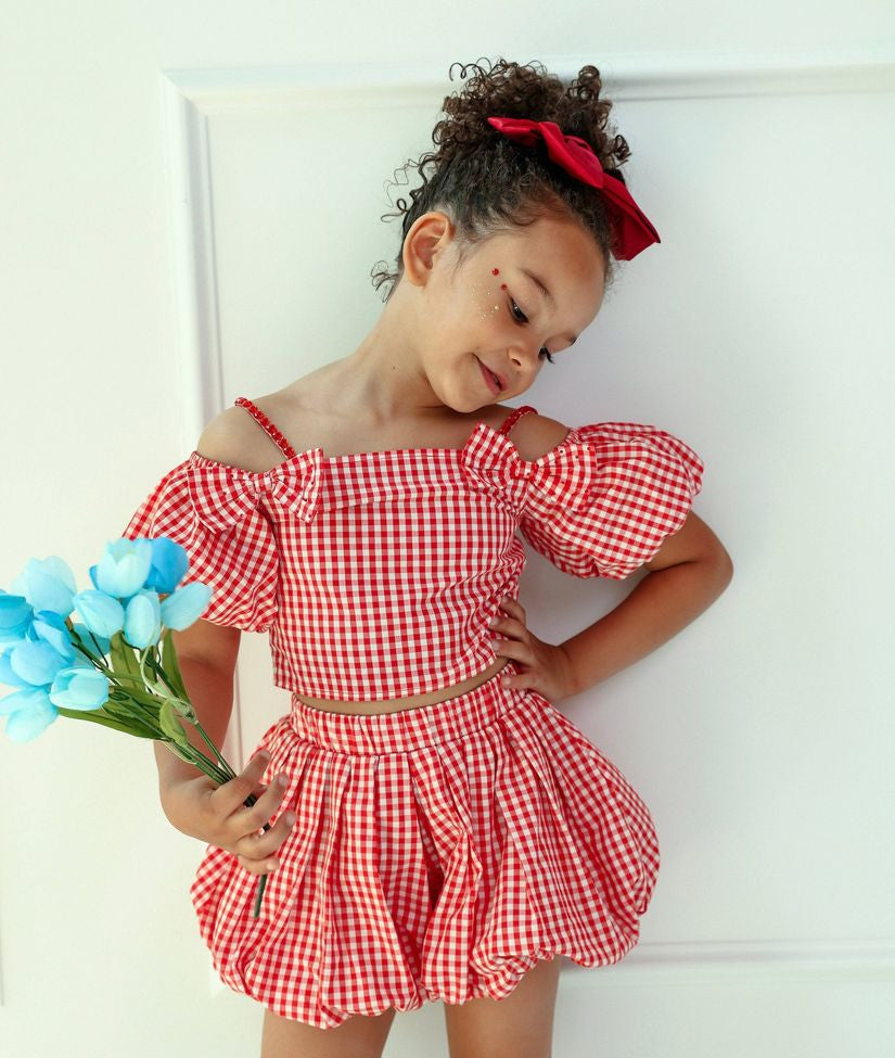 Young girl in a red checkered dress holding blue flowers against a white background