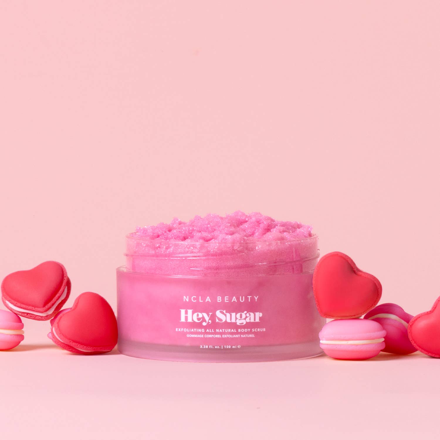 Pink body scrub jar with heart-shaped containers on a pink background