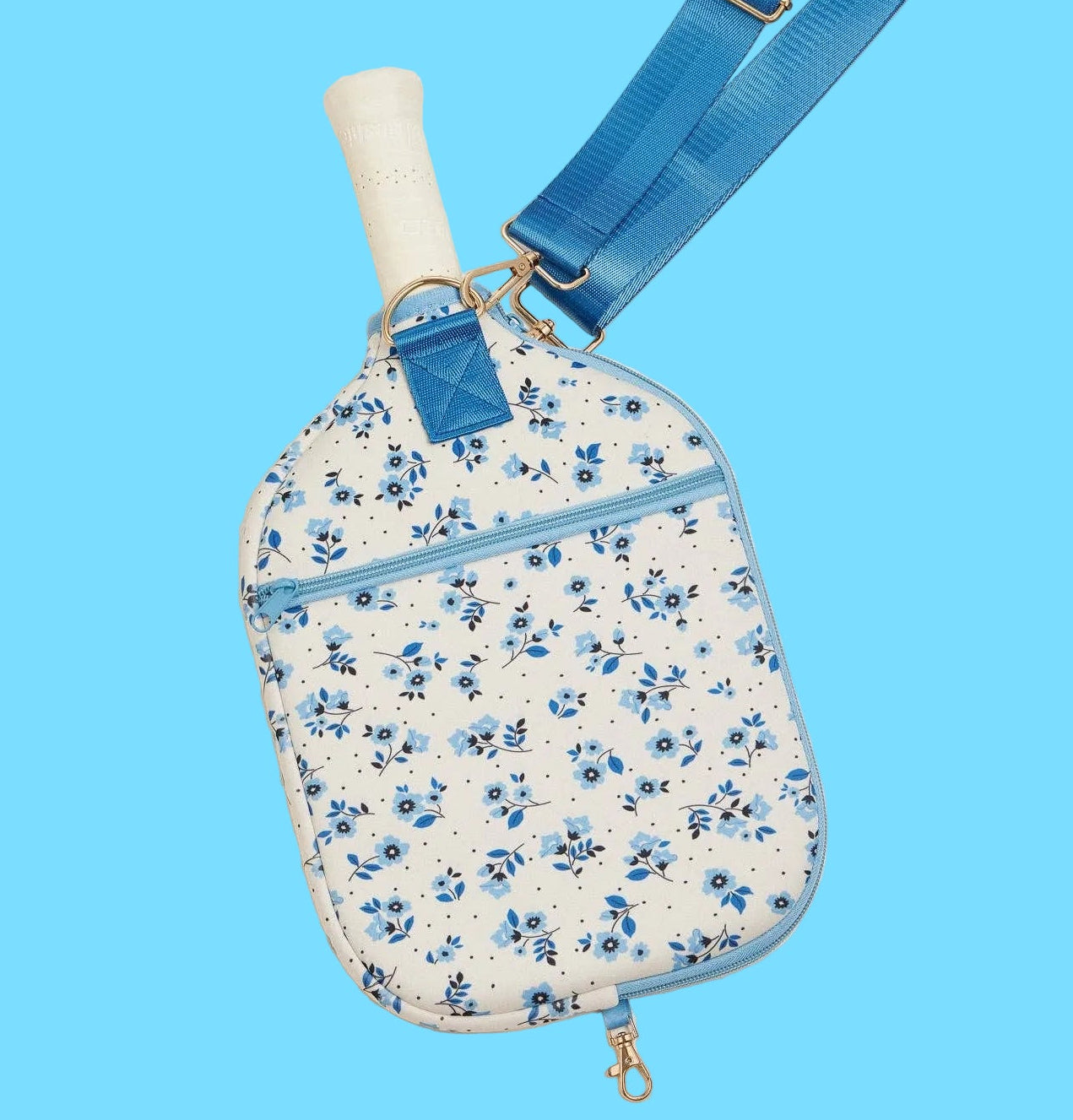 Floral-patterned crossbody bag with blue strap on a light beige background