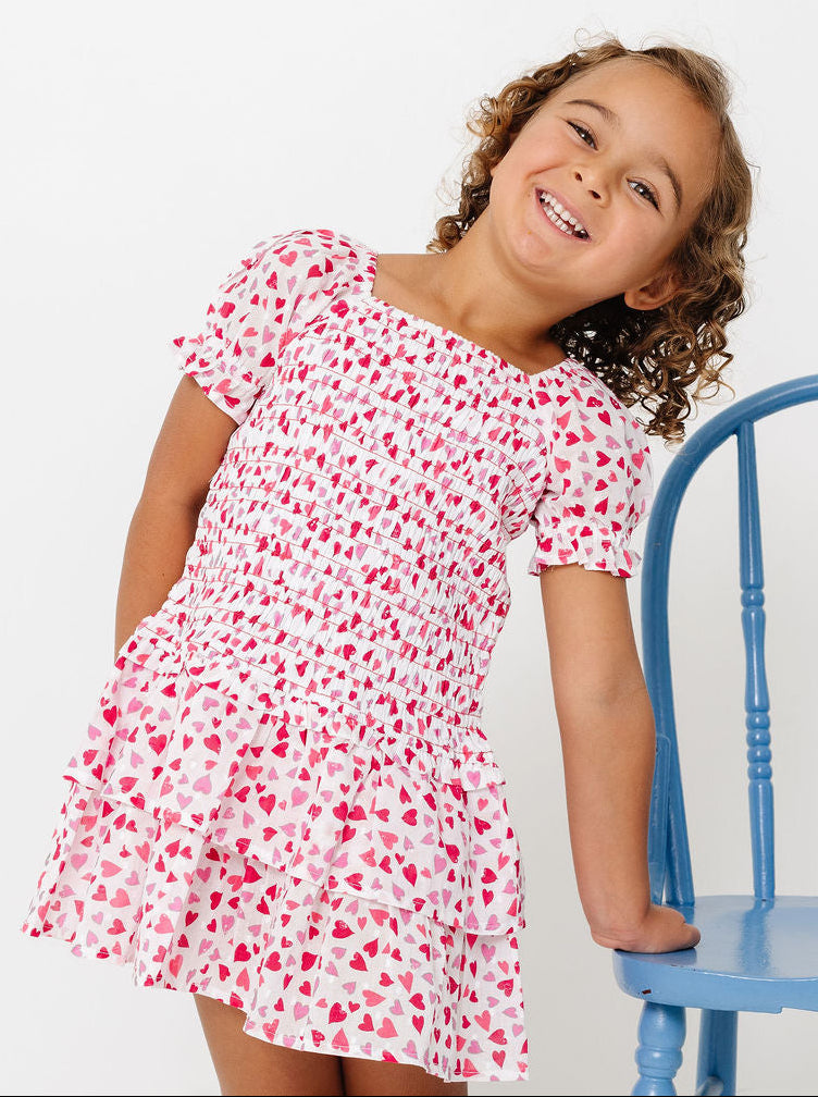 Young girl in a pink floral dress standing next to a blue chair against a white background