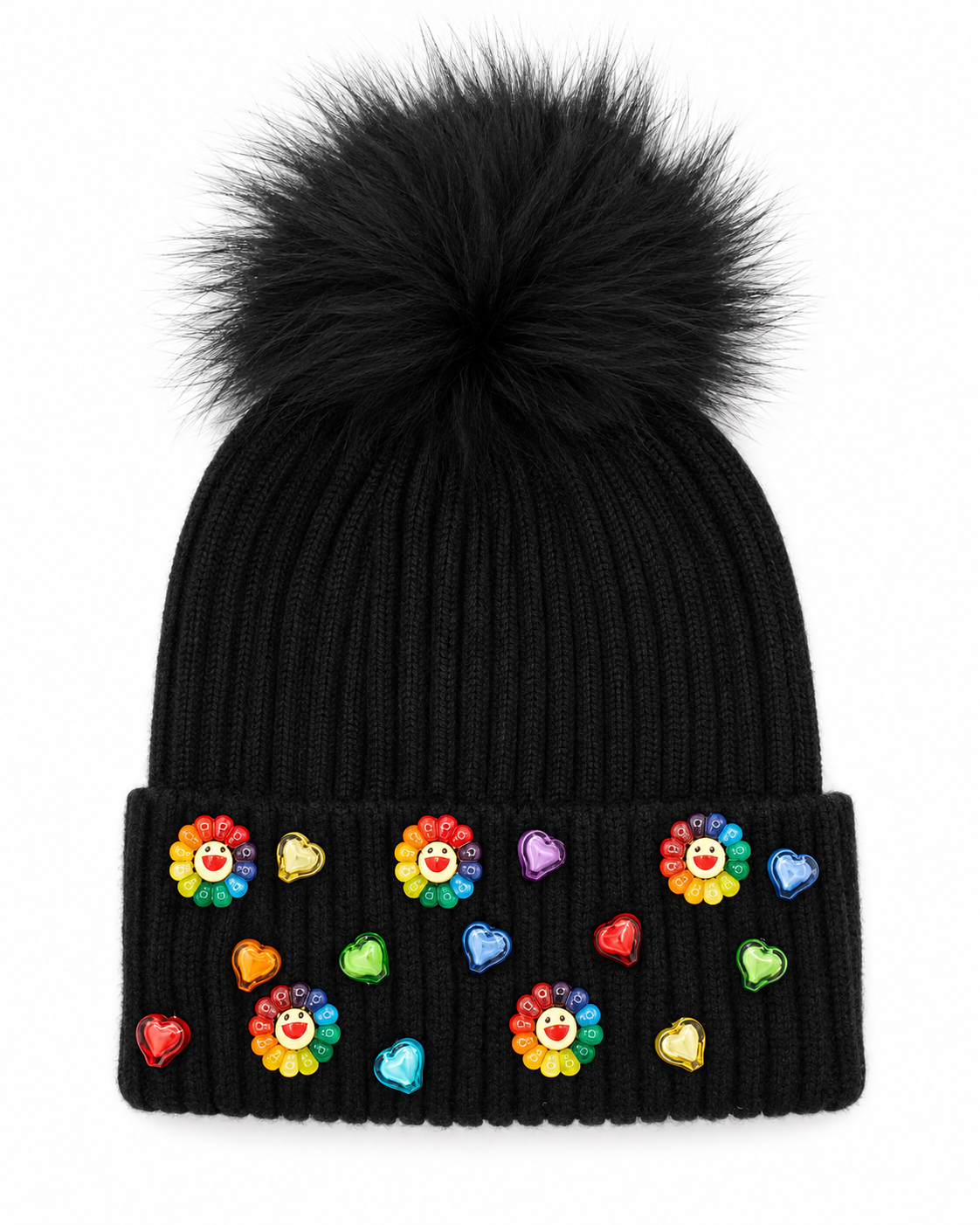 A black ribbed knit winter hat with a large fluffy black fur pom on top and colorful rainbow daisy and heart charms decorating the front cuff.