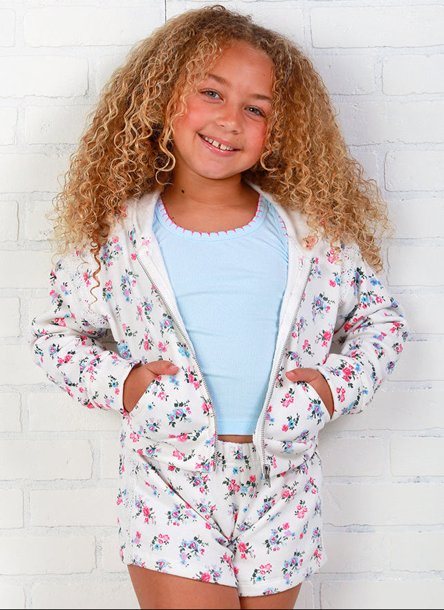 girl wearing a flowers by zoe floral print outfit against a white brick wall 