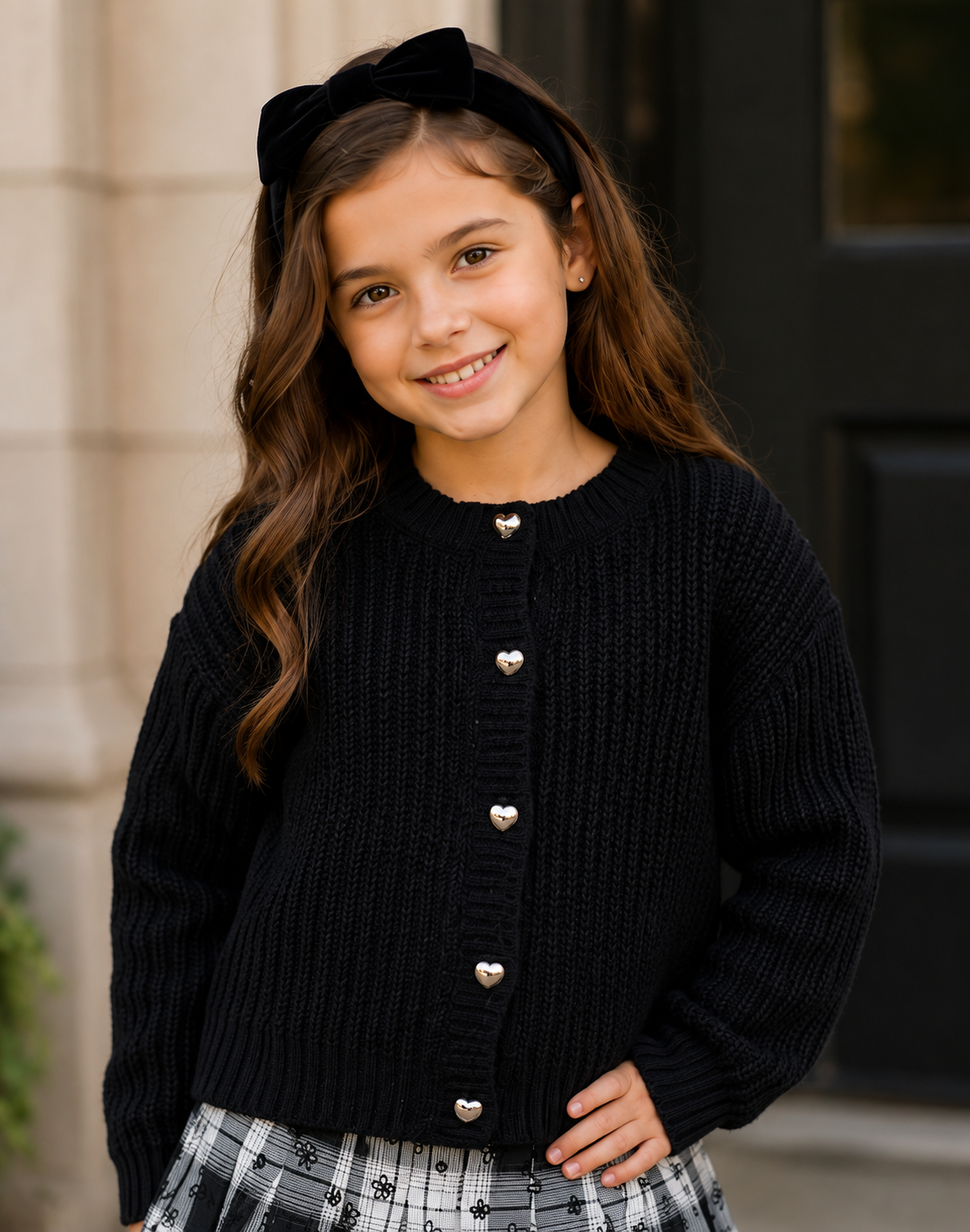 Tween girl wearing a black knit cardigan with heart buttons
