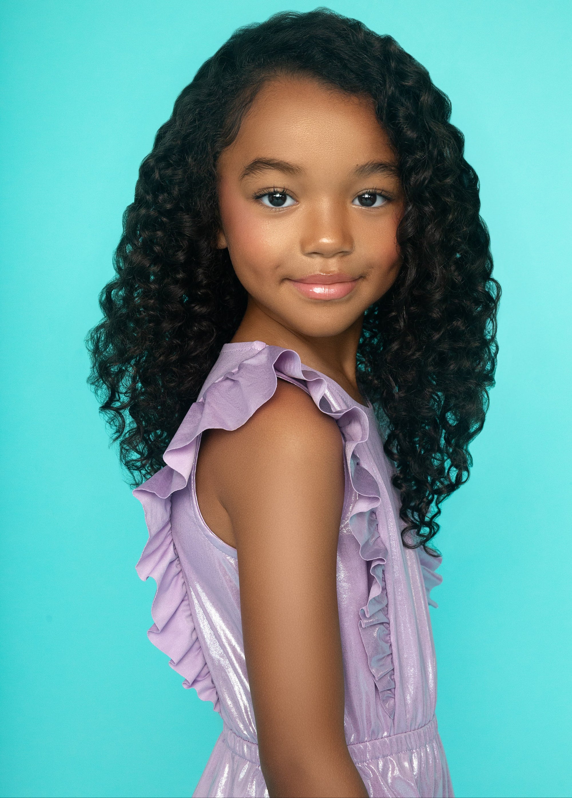 Young girl with curly hair wearing a purple dress against a blue background