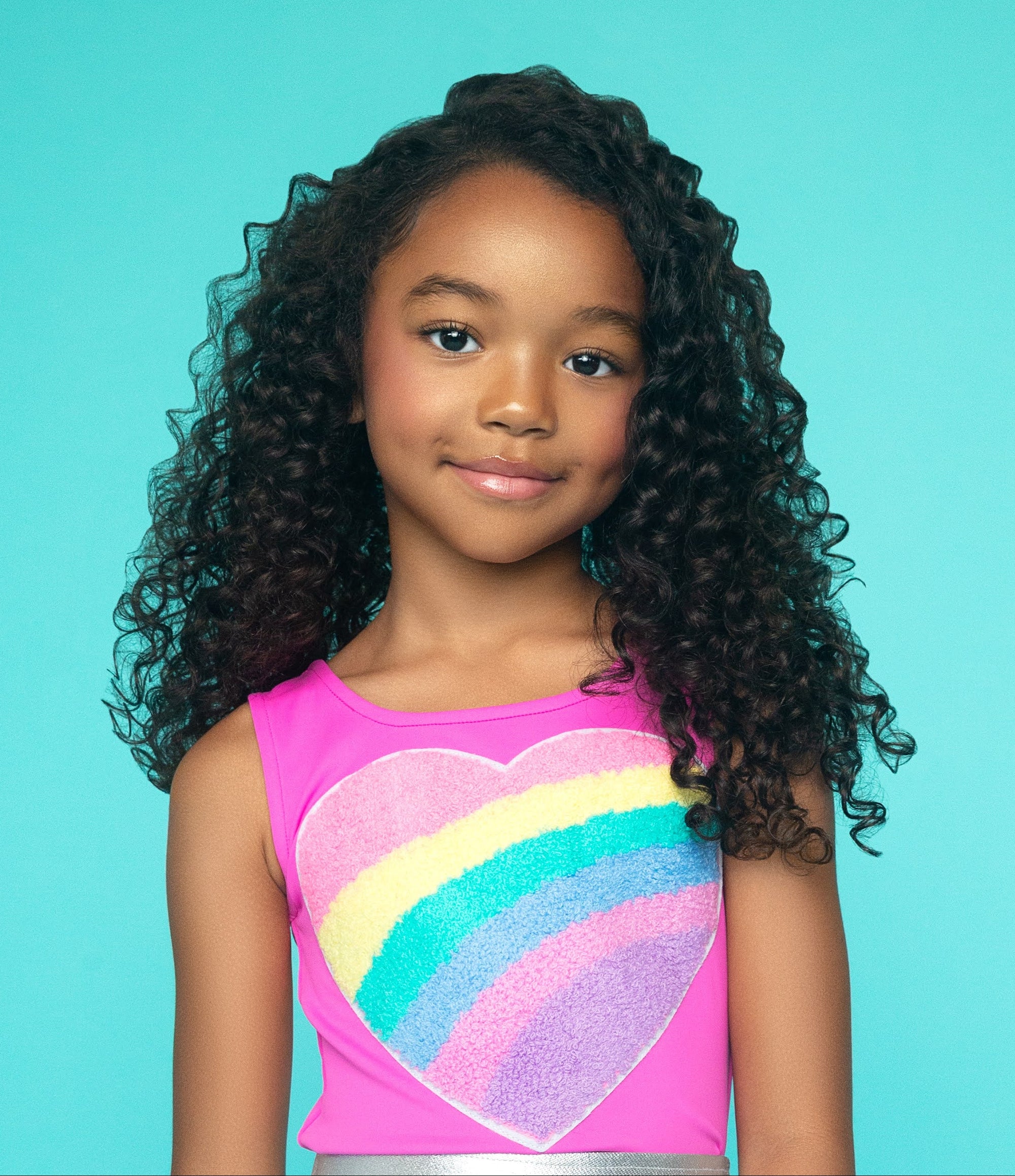 Young girl wearing a colorful heart top and silver skirt with rainbow designs on a blue background