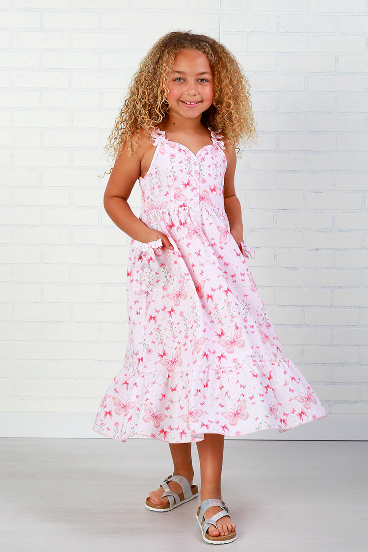 Young girl wearing a pink floral dress against a white brick wall.