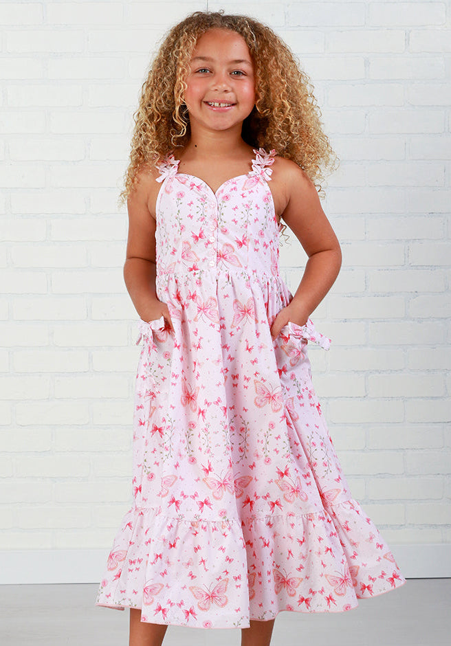Young girl wearing a pink floral dress against a white brick wall.