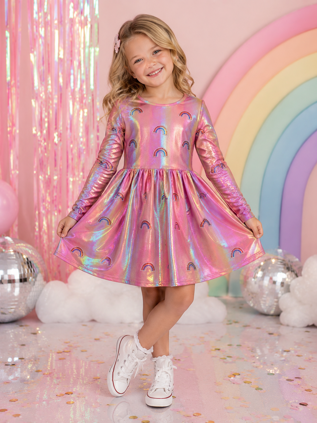 Little girl wearing the Rockwilde pink metallic rainbow dress with sparkling rhinestone rainbow appliqués and long sleeves.