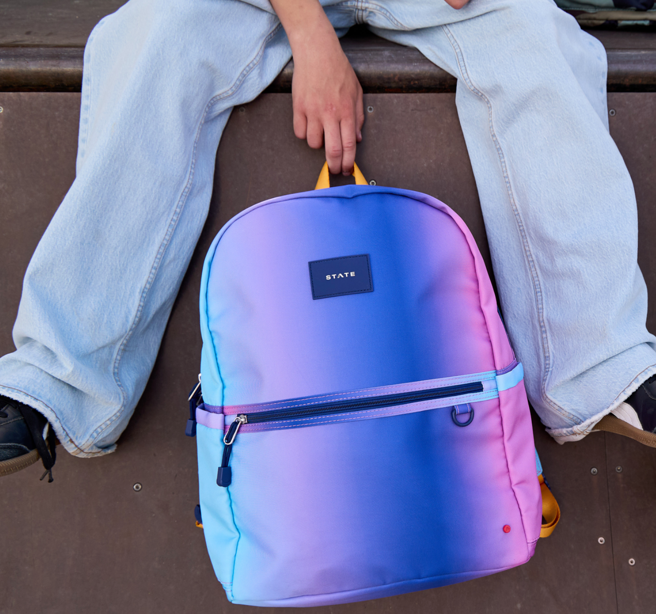 Front view of the STATE Bags Kane Double Pocket Large Backpack featuring a vibrant blue, purple, and pink gradient design