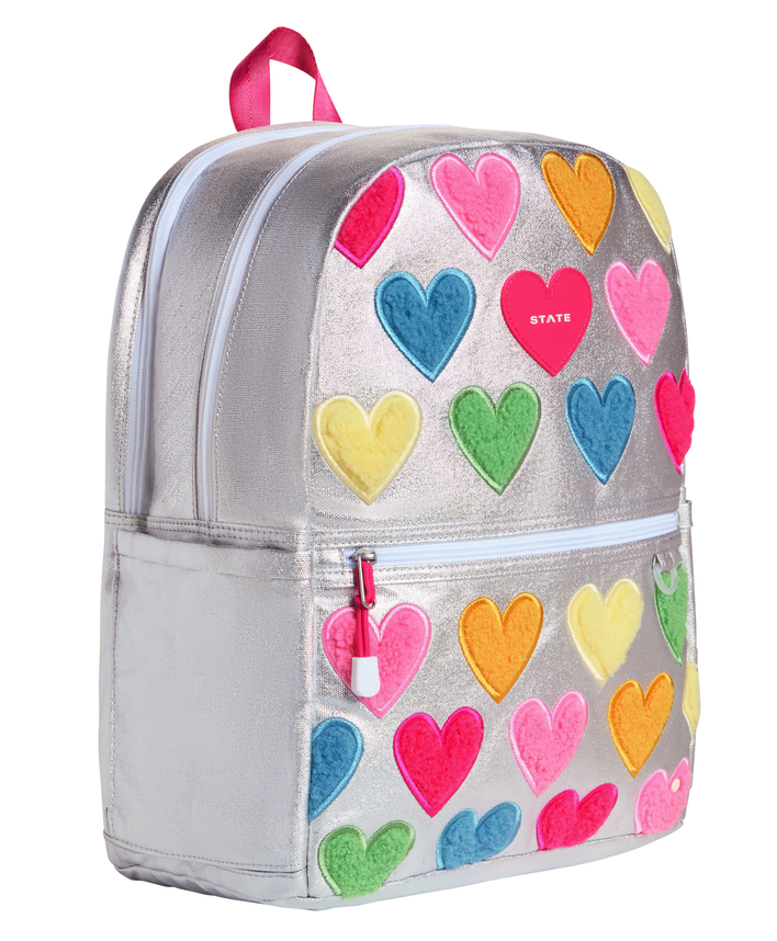 Angled view of the STATE Bags Happy Chenille Hearts backpack showcasing spacious double compartments, front organization pocket, and premium metallic finish