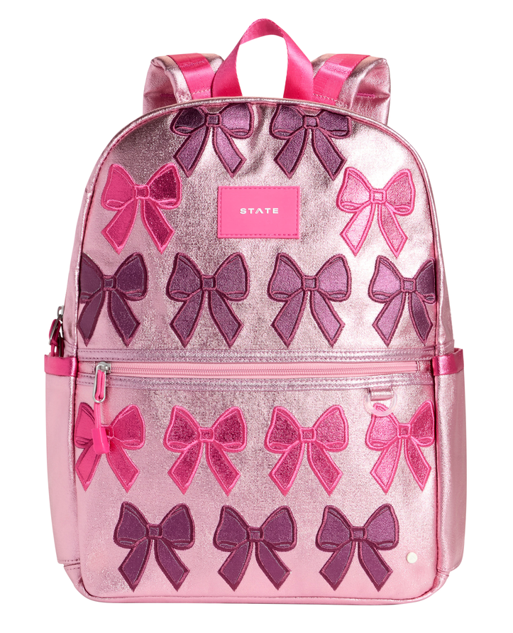 Front view of the STATE Bags Kane Backpack in Metallic Bows featuring dimensional pink bow appliqués on a shimmering metallic pink background.
