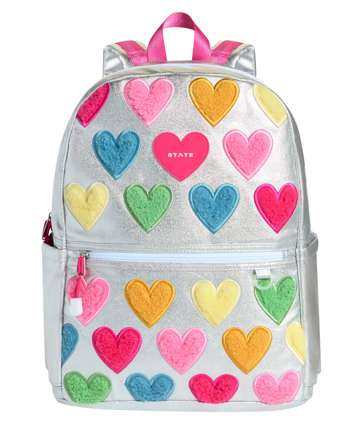 Front view of the STATE Bags Kane Double Pocket Backpack in Happy Chenille Hearts featuring colorful chenille heart appliqués on a shimmering metallic silver background.
