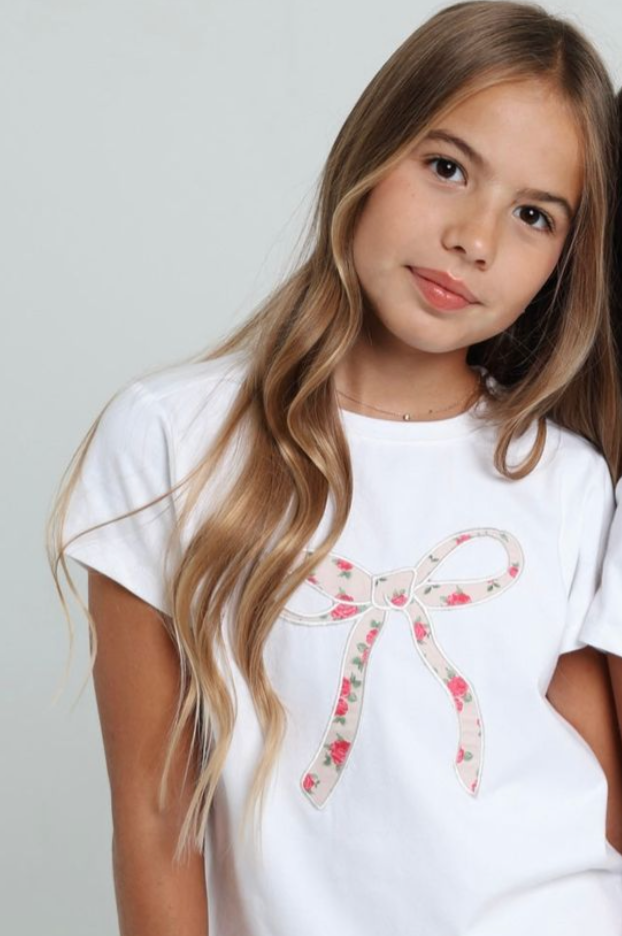 Young girl wearing a white t-shirt with a floral design on a plain background