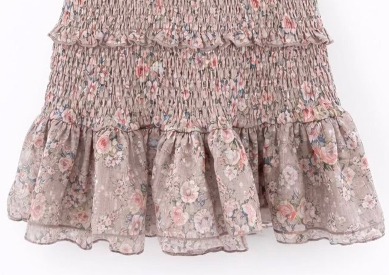 Close-up of a smocked floral skirt with tiered ruffles in a dusty pink, beige, and blue floral pattern against a white background.
