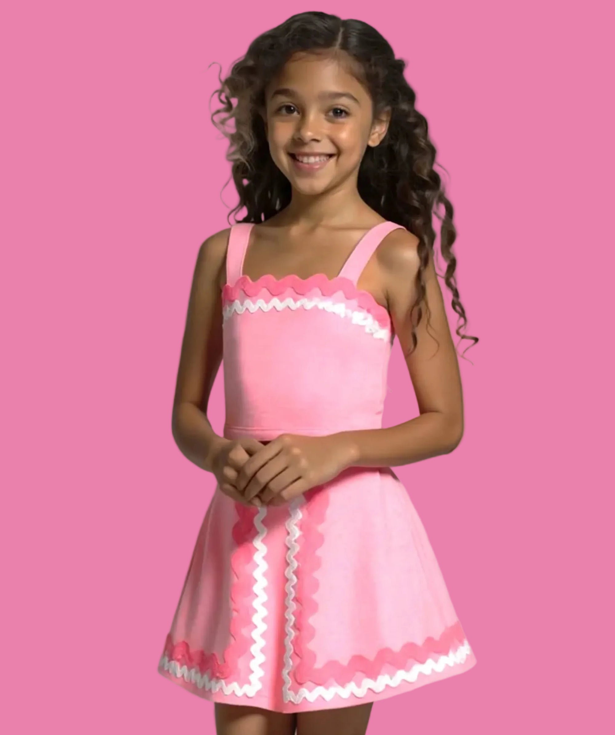 Young girl wearing a pink dress with white trim against a pink background