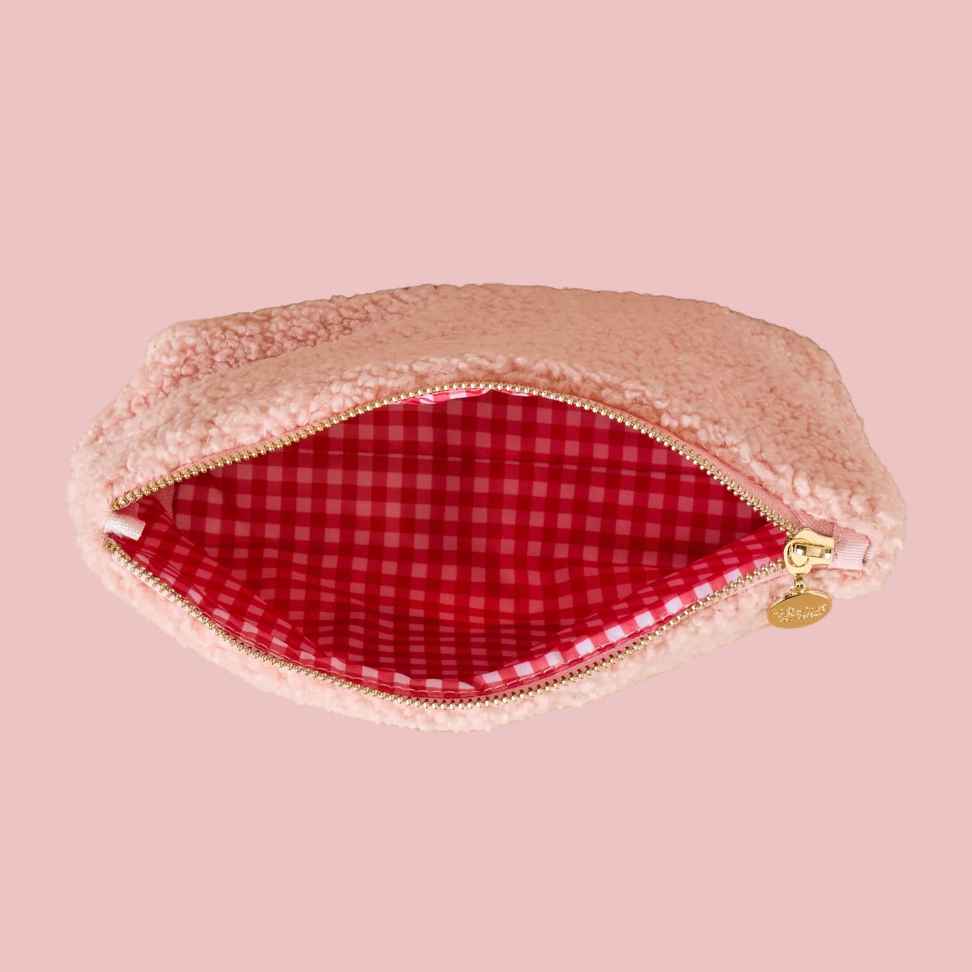Pink fuzzy makeup bag with red checkered interior on a beige background
