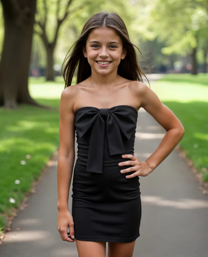Young girl wearing a black strapless dress with a bow in a park setting