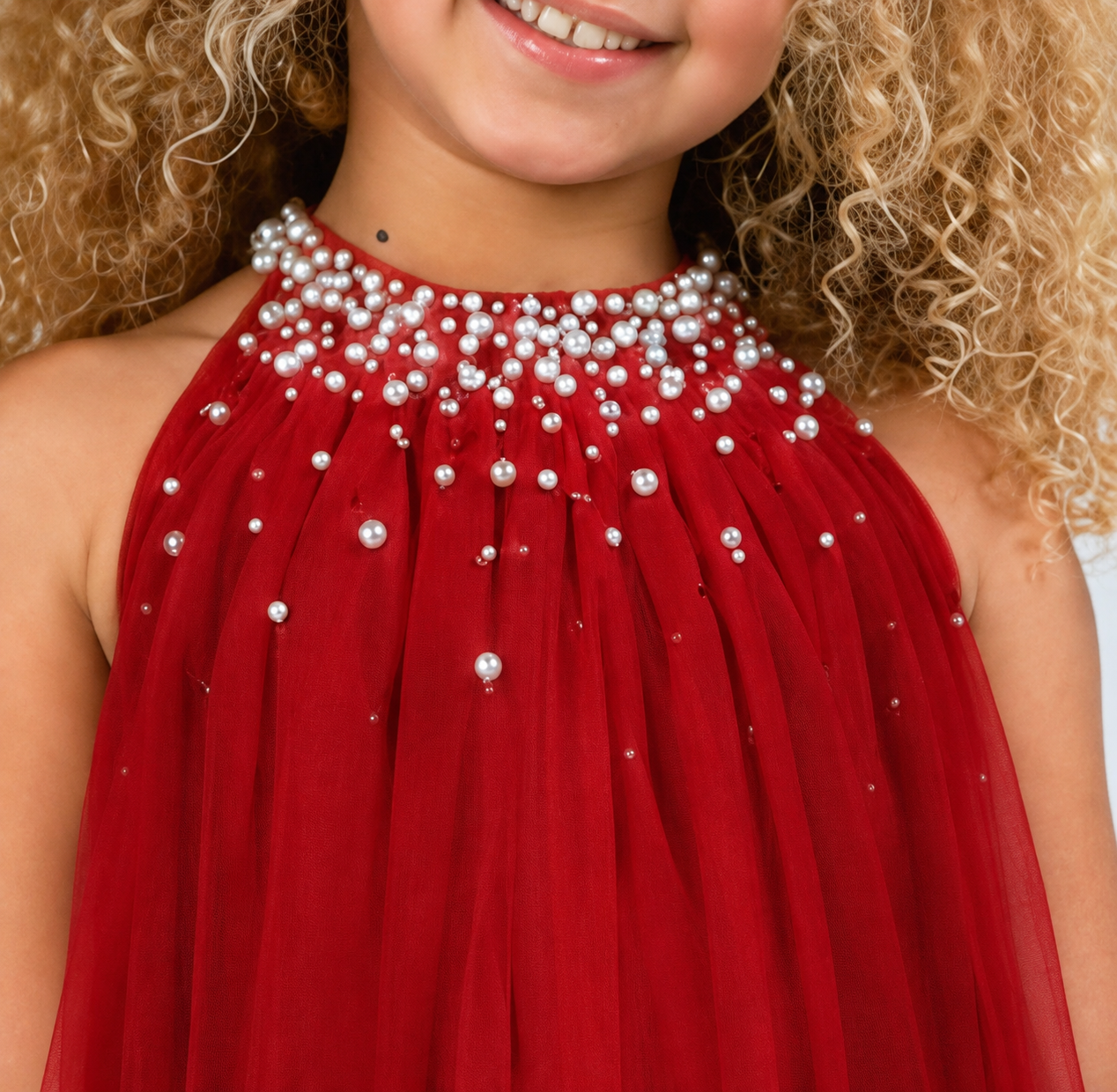 A close-up of a child wearing a sleeveless red dress with a high neckline heavily embellished with white pearl-like beads and small silver beads.