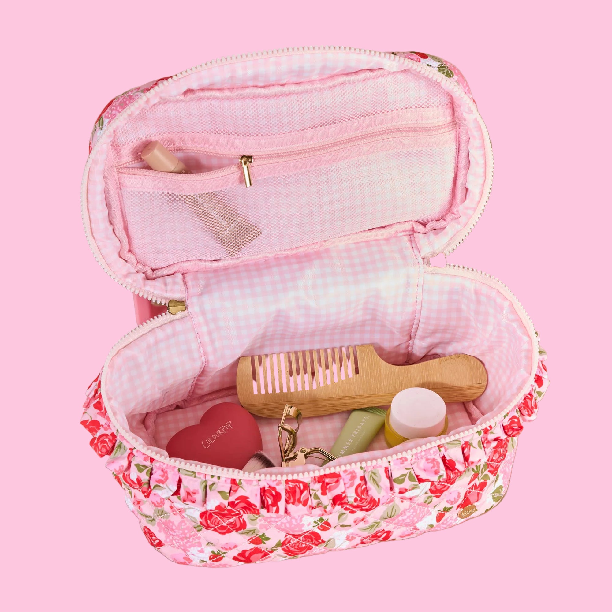 Pink floral travel case with toiletries on a beige background