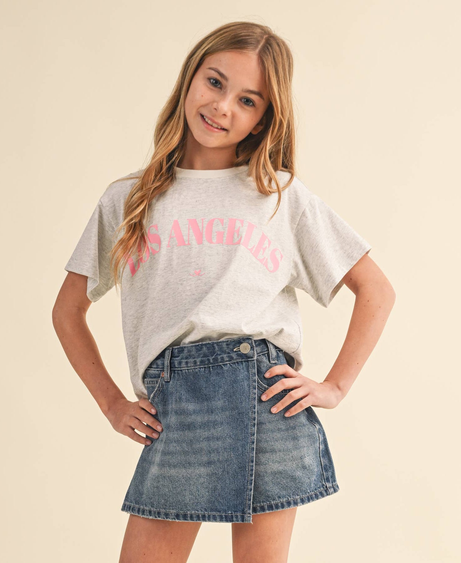 Young girl wearing a white t-shirt with text and a denim skirt on a beige background