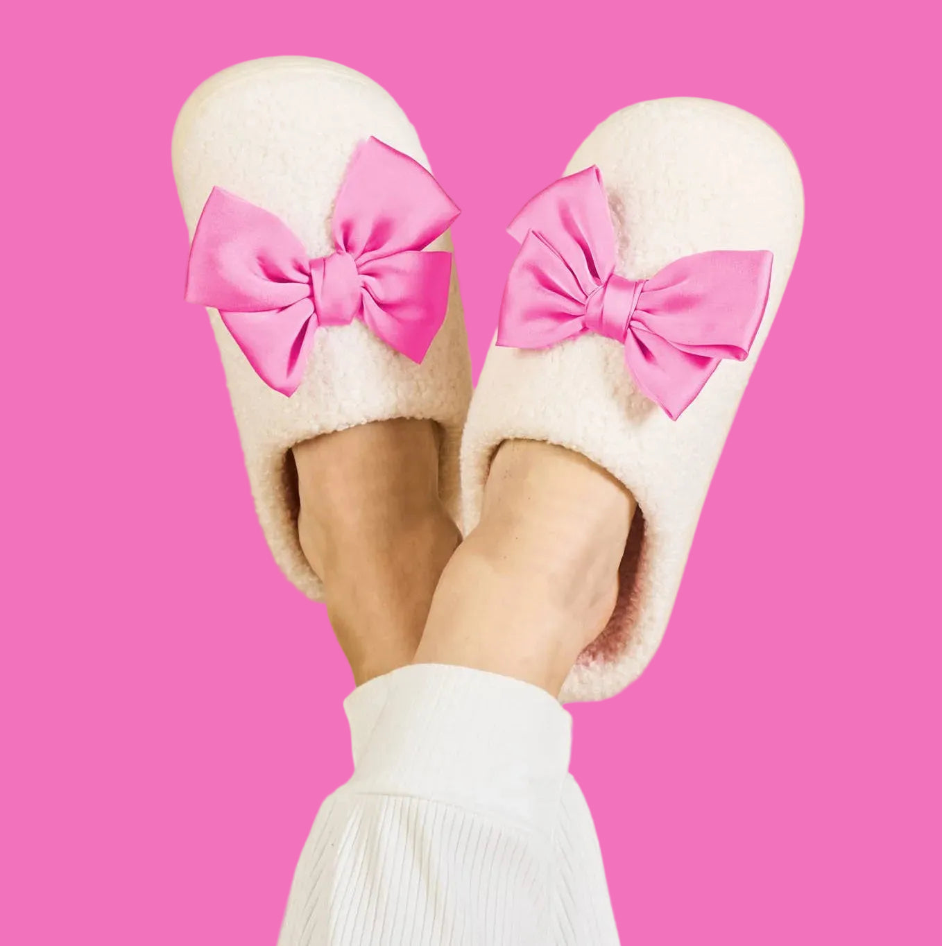 White slippers with pink bows worn by a person on a beige background