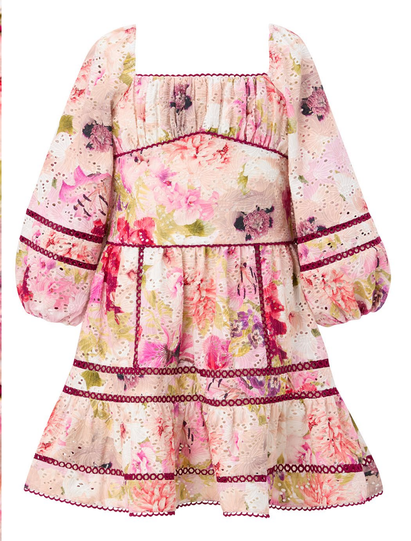 A girls tiered off-the-shoulder dress with a pink, red, and green floral print on a cream base, featuring dark red embroidered trim details.