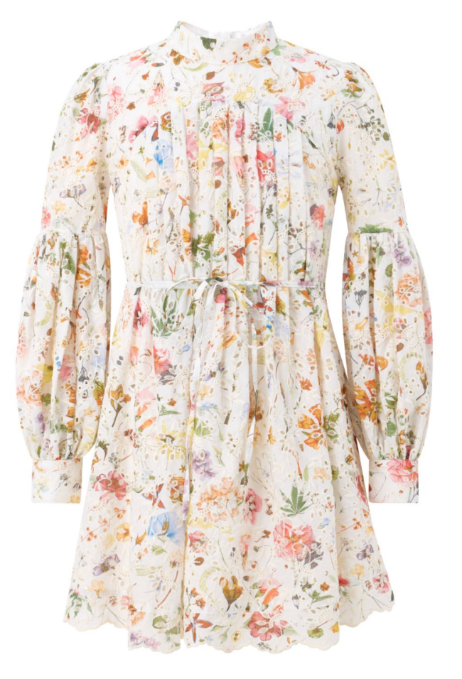 A long-sleeve, high-neck girls mini dress with a gathered waist and an all-over pastel floral print on a cream background, shown against a plain white background.