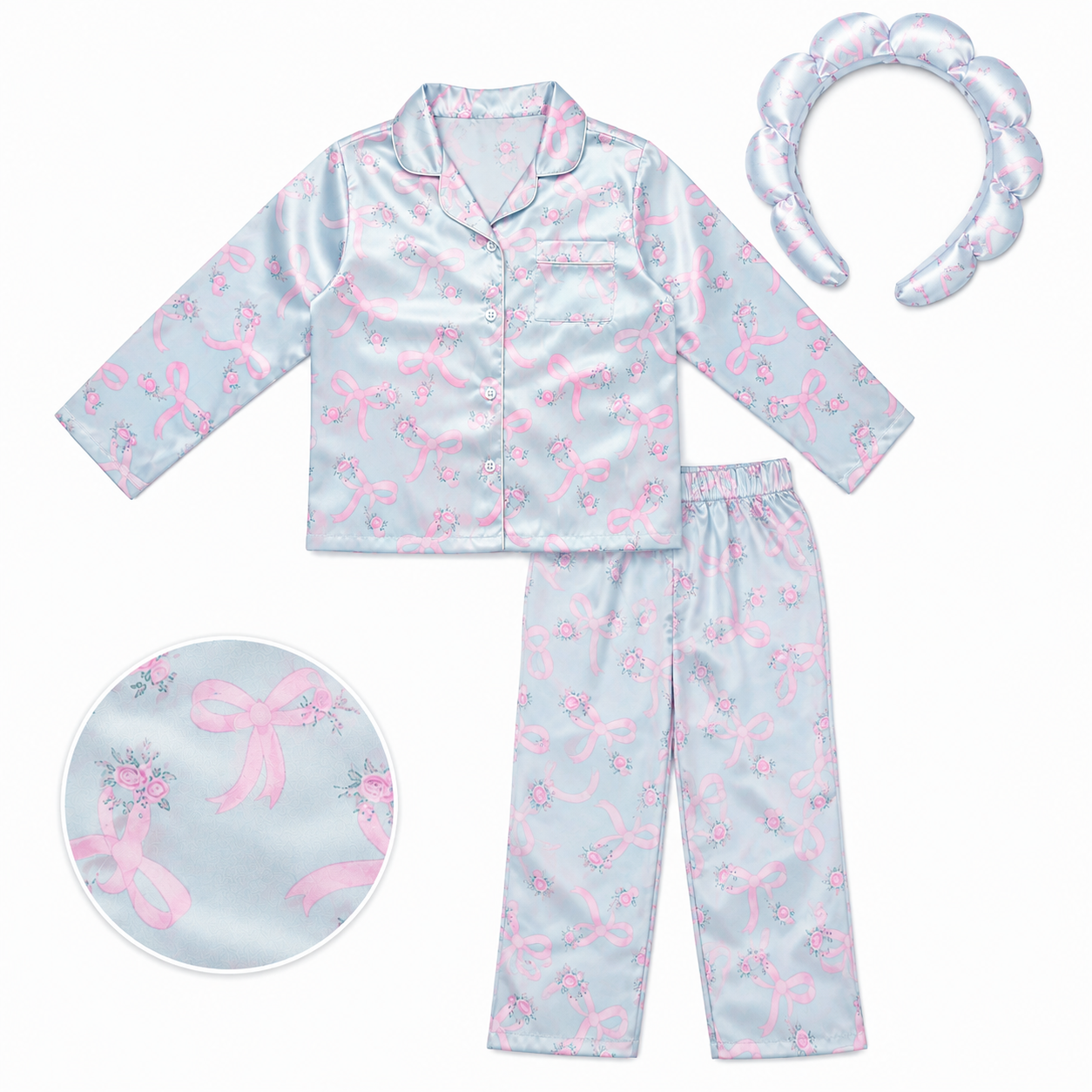 A two-piece girls' pajama set in light blue satin with a pink bow pattern, including a long-sleeve button-up top and matching pants, shown with a matching pink bow headband on a white background.