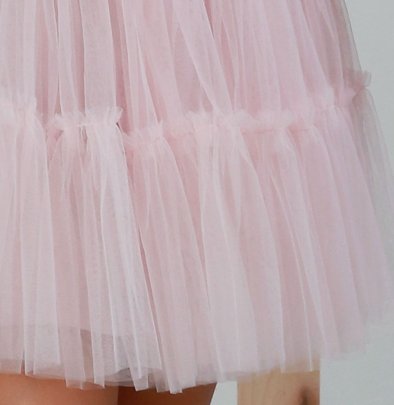 Close-up of a light pink tulle skirt with ruffled tiers and sheer layered fabric.