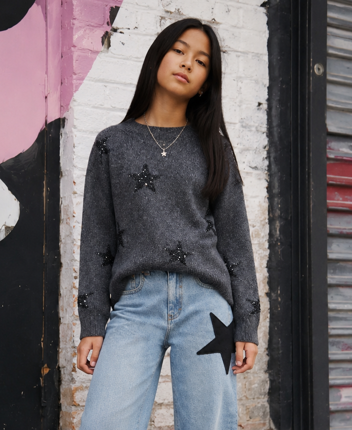 Tween girl wearing charcoal gray sweater with black sequin stars styled with wide-leg denim.